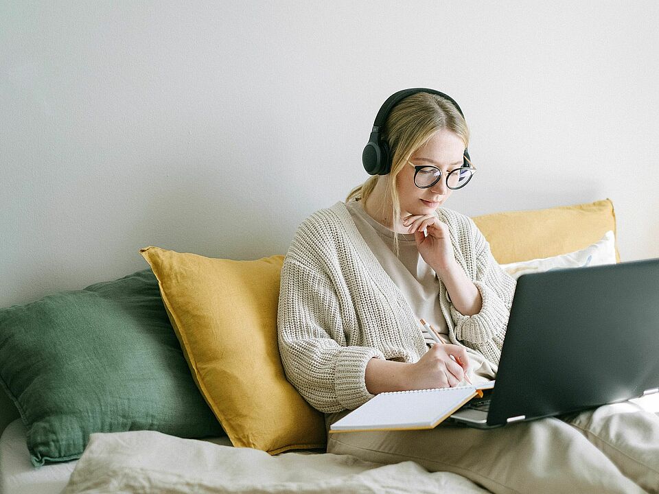 Frau mit Kopfhörer und Laptop auch Sofa macht Notizen