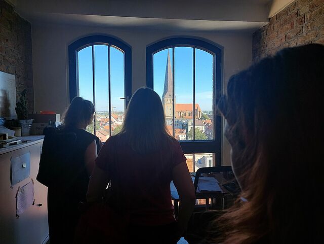 Studierende stehen vor einem hochgelegenen Fenster und schauen auf Kiel
